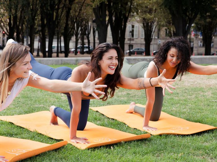 Une pratiquante en posture de yoga, bras levés, sur un toit ensoleillé.
